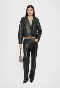 Črna usnjena motoristična jakna, pletena zlata pulover, črne usnjene hlače, drži majhno kovinsko torbico, v pointed black heels.