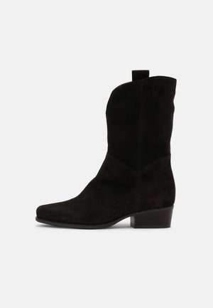 Botte mi-mollet en daim noir avec talon bas et épais, bout pointu et languette à l'arrière du col, présentée sur fond blanc.