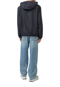 Marineblauwe lichtgewicht jas met een capuchon, elastische zoom en casual pasvorm. Draag het boven lichtblauwe baggy jeans en witte sneakers.