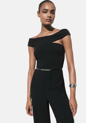 Black off-shoulder top with a cutout detail, made of smooth fabric, featuring a fitted design and a silver-tone belt accent.