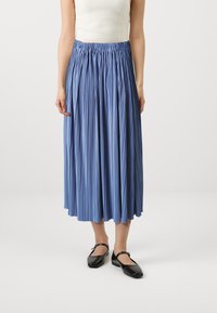 Lyseblå, plisserte midi-skirt med elastisk midje. Laget av glatt stoff, med vertikale plisseringer og flytende design. Sorte, patentlær Mary Jane-sko.