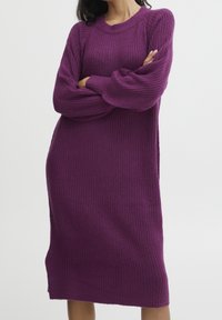 Abito a maglia viola con texture a coste e maniche lunghe, dotato di scollo rotondo e spacchi laterali per facilitare i movimenti.