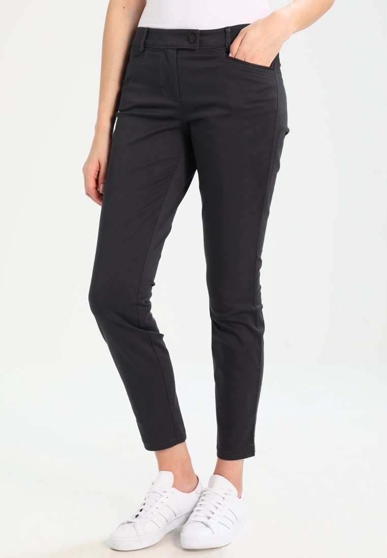 Czarne spodnie slim fit wykonane z miękkiego materiału, z przednimi kieszeniami, zapięciem na guzik i zwężanymi nogawkami, w połączeniu z białymi sneakersami.