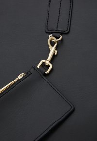 Schwarze Ledertasche mit einem goldenen Metallschnappverschluss, einer Reißverschlusstasche und aufwendigen Nähten an den Rändern. Eine strukturierte Oberfläche ist sichtbar.