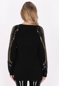 Pulover negru cu mâneci lungi, decorat cu dungi din paiete aurii și argintii pe mâneci. Material tricotat moale, croială lejeră și guler rotund.