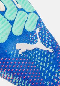 Parte superiore della scarpa sportiva blu con accenti in gomma verde e superficie texturizzata. Presenta un logo Puma bianco, motivi intricati e un design che aderisce perfettamente.