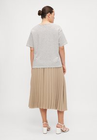 Stripet kortermet topp i hvit og svart, kombinert med en plisserte beige skjørt som går til kneet, og hvite hælesandaler.