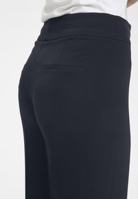Black pants made from a smooth fabric, featuring a flat waistband, back pocket, and a tailored fit, with minimal visible stitching.