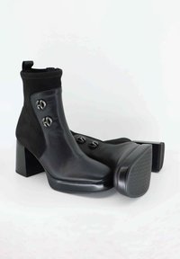 Stivaletti neri che presentano una combinazione di pelle e camoscio, tacco a blocco spesso e due bottoni metallici decorativi sui lati. Sole in gomma texturizzata.