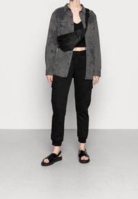 Grå tie-dye skjorta med knappar över en svart crop top, i kombination med svarta cargobyxor och svarta slidesandaler, samt en svart crossbody-väska.