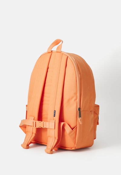 Zaino in tessuto arancione con spallacci imbottiti, manico superiore, tasche con zip e fibbie regolabili. Presenta una superficie liscia e testurizzata.