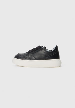 Svart lädersneaker med vit gummisula, rund tå, svarta snören och subtila sömdetaljer på ovandelen. Enkel, lågprofil design.
