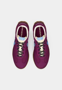 Purple textile sneakers with black laces, light blue accents, and cream lining. Rubber soles with a textured grip pattern.