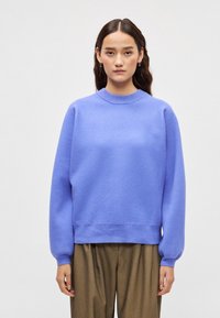 Μωβ πλεκτό πουλόβερ με στρογγυλή λαιμόκοψη, μακριά μανίκια και ριμπ μανσέτες. Φοριέται πάνω από καφέ παντελόνια με ψηλή μέση. Απαλή υφή.