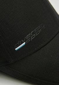 Czarna czapka sportowa wykonana z teksturowanej tkaniny. Posiada małe logo w szarym kolorze oraz niebieską akcentującą linię. Zakrzywiony daszek i widoczne przeszycia.