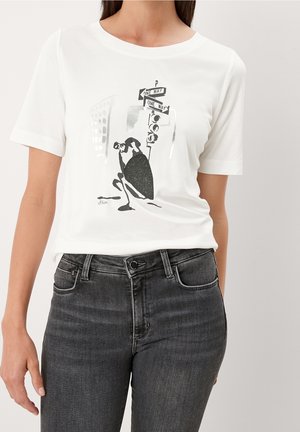 Femme portant un t-shirt blanc avec un graphique en noir et blanc représentant une silhouette accroupie près de panneaux de rue à sens unique et de feux de circulation.