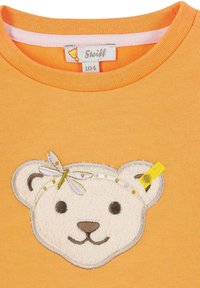 Oranje katoenen t-shirt met een gestructureerd wit berenhoofd met geborduurde details, waaronder een gele accent en twee antennes.