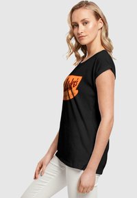Musthave must-valged lühikeste varrukatega T-särk, mis on valmistatud puuvillast. Ees on oranž graafiklogo keskel. Sujuv tekstuur ja mugav lõige.