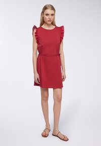 Abito in cotone rosso con maniche corte a volant, vita aderente e vestibilità rilassata. Abbinato a sandali piatti marroni. Design semplice e moderno.