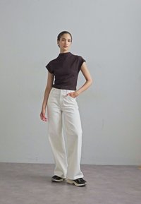 Haut marron à col montant et manches courtes associé à un pantalon large blanc et des baskets noires. Texture lisse, coupe décontractée, design minimaliste.