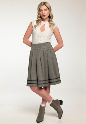 Weiße Spitzenbluse mit Schlüssel-Ausschnitt, grauer Plisseerock mit schwarzen Streifen und graue Ankle-Boots mit niedrigem Absatz.