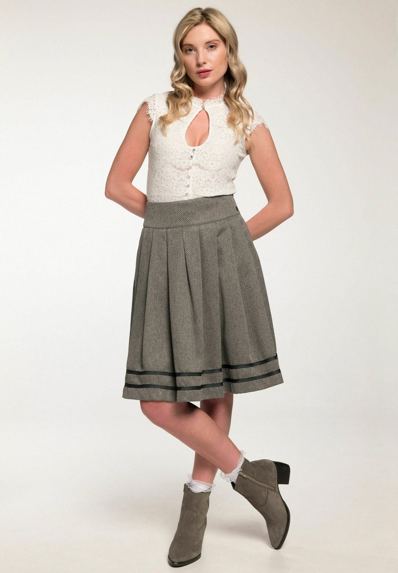 Witte kanten blouse met sleutelgat, grijze geplooide rok met zwarte strepen en grijze enkellaarsjes met een lage hak.