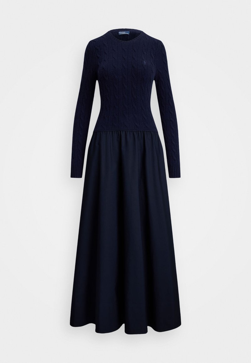 Vestido azul marino con un cuerpo de punto trenzado y una falda fluida. Manga larga, escote redondo y detalle de cintura fruncida. Textura de tela suave.