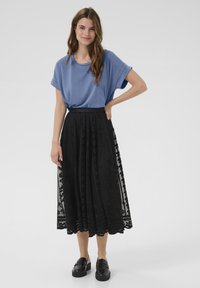 Mėlyna trumpa rankovė viršūnė, derinama su juoda ilga suknele, kuri turi nėrinių detalizavimą ir išlenktą kraštą, dėvima su juodais loaferiais.