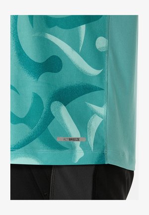 Lyhythelmainen urheiluoppe, jossa on teal-värinen abstract-kuviointi tummemmissa sävyissä. Tässä on heijastava ACTIBREEZE-tunnus lähistöllä saumaa.