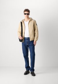 Bežna zip-up jopica s kapuco, bela majica, temno modri ravni kavbojki, črni loafers in črne pravokotne sončne očala.
