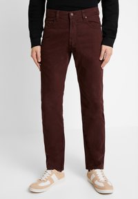 Pantaloni chino bordeaux con vestibilità slim, realizzati in tessuto misto cotone, con cinque tasche e chiusura con bottone, abbinati a sneakers beige.