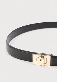 Melns ādas josta ar gludu tekstūru, kas aprīkota ar taisnstūrveida zelta toņa sprādzi ar izteiktu aizslēgšanas mehānismu.