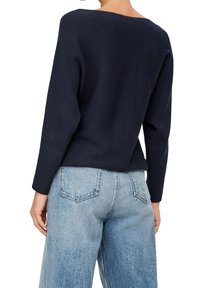 Suéter de punto acanalado azul marino con escote ancho y mangas largas, combinado con pantalones vaqueros de pierna ancha en azul claro.