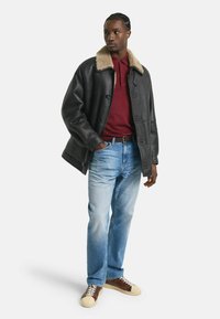 Veste en cuir noir avec un col en shearling beige, associée à un polo bordeaux, un jean bleu clair et des baskets marron et crème.