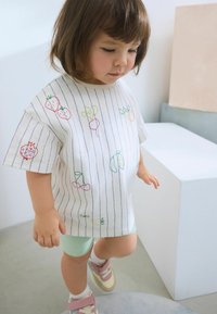 Hvidstribet T-shirt med farverig frugt broderi, korte ærmer, afslappet pasform, parret med lysegrønne shorts og multicolor sneakers.