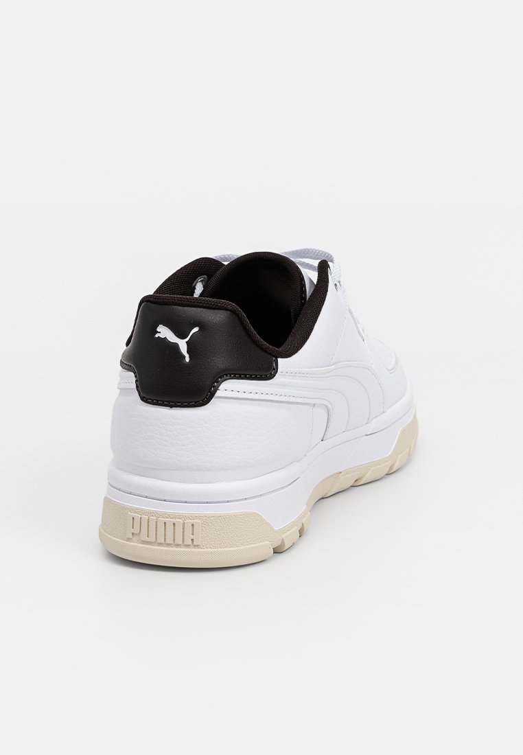 Białe sneakersy z teksturowanym skórzanym wierzchem, czarnym akcentem na pięcie i beżową gumową podeszwą; posiadają wyraźne logo Pumy na pięcie.