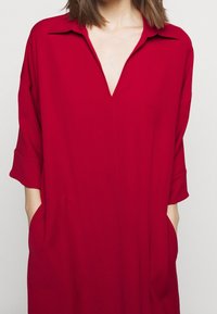 Robe tunique rouge avec un décolleté en V profond, des manches courtes et des poches latérales. Confectionnée dans un tissu lisse avec une coupe ample et décontractée.