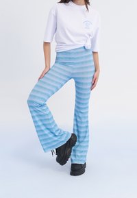 Blå vida byxor med ett zigzag-mönster i olika nyanser av blått, tillverkade av stretchigt material. Bärs med en vit t-shirt och svarta skor.