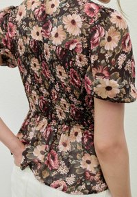 Blommig blus med en mörk bakgrund och rosa samt krämfärgade blommor, smockad byst och puffärmar. Mjuk, lättviktsmaterial.