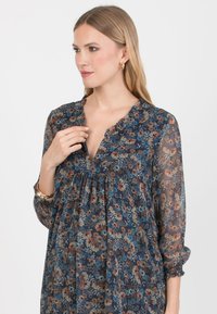 Kwiatowa sukienka charakteryzuje się ciemnoniebieską przezroczystą tkaniną z kolorowymi wzorami kwiatowymi, falbanowym dekoltem oraz marszczeniami w okolicy biustu.