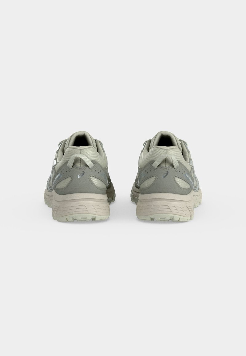 Par de zapatillas para correr de color gris claro y beige vistas desde atrás sobre un fondo blanco liso.