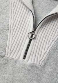 Grauer Pullover mit einem Viertelreißverschluss, der ein strukturiertes Ripppanel und einen glatten Fleece-Körper aufweist, silberne Beschläge am Reißverschluss.