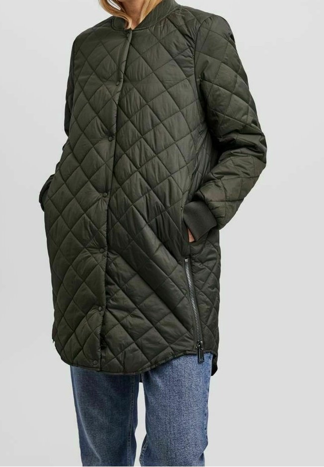 Veste matelassée de couleur vert foncé, longueur moyenne, avec boutons-pression, détail de fermeture éclair latérale, poignets côtelés, portée sur un jean bleu.