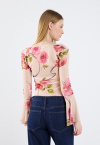 Haut à manches longues floral en tissu transparent avec des roses roses sur un fond clair, doté de manches évasées et d'une silhouette ajustée.