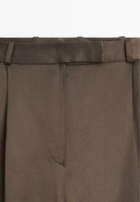 Bruine linnen broek heeft een vlakke tailleband, scherpe plooien en een subtiele glans. Ze hebben een opening voor een voorkeurszak en minimale stikdetails.