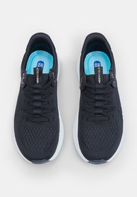 Chaussures de sport noires avec une tige en mesh texturé, des lacets plats et une semelle intérieure bleu clair, présentant une semelle blanche et des accents de logo.