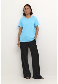  Lichtblauwe t-shirt met korte mouwen, relaxte pasvorm, ronde halslijn, gecombineerd met zwarte wijde pantalon en zwarte platte sandalen. Eenvoudig, casual ontwerp.