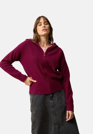 Maroon zip-up hoodie med ribbat tyg, långa ärmar, huva och sidfickor, kombinerad med en grå denimkjol.