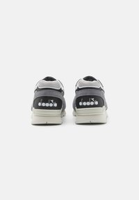Scarpe da ginnastica grigie con pannelli laterali testurizzati, accenti bianchi e un logo nero sul tallone. Suola grigia chiara con motivo del battistrada.