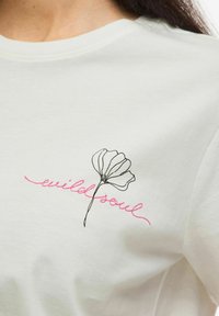 Bawełniany t-shirt w kremowym kolorze z czarnym rysunkiem linii kwiatu oraz różowym haftowanym napisem „wild soul” na dolnej lewej stronie.